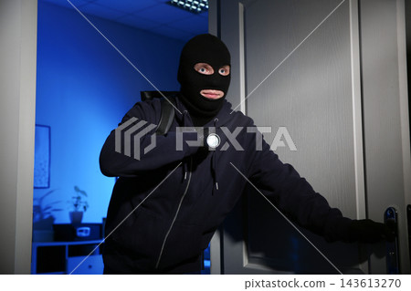Thief with flashlight breaking into house at night Thief with flashlight breaking into house at night 143613270