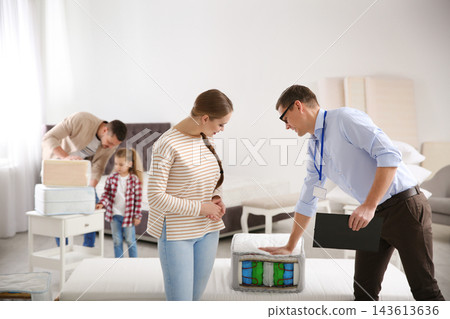 Salesman showing young woman section of mattress in store Salesman showing young woman section of mattress in store 143613636