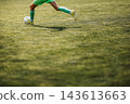 Cropped view of a soccer player in a green uniform running with the ball on a sunlit grass field, with open copy space in the foreground. 143613663