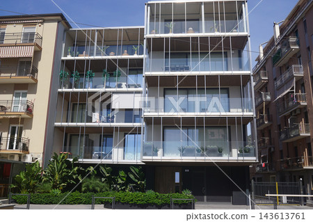 Modern four-story apartment building featuring panoramic balconies, floor-to-ceiling windows, lush greenery, and contemporary architectural design in a stylish residential setting. Modern four-story apartment building featuring panoramic balconies, floor-to-ceiling windows, lush greenery, and contemporary architectural design in a stylish residential setting. 143613761