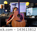 Woman musician hiding her face with an acoustic guitar in a recording studio 143613812