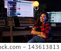 Smiling and confident woman composer sitting in a chair next to a mixing console 143613813