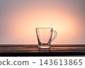 Empty transparent glass tea cup with handle sitting alone on a table. Clean minimalist composition on a soft light pink background. 143613865