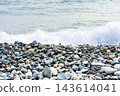 Ocean wave breaking onto a pebble beach. Rocky shoreline with surf and open water. Coastal nature and seascape. Copy space for travel and environmental design. 143614041