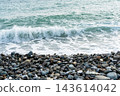 Ocean wave breaking onto a pebble beach. Coastal seascape and natural shoreline. Sea water movement, surf and erosion. Tranquil nature background with textured stones 143614042