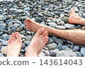 Bare feet resting on smooth pebbles at a rocky beach. Relaxation and leisure by the shore. Summer vacation and coastal recreation. Natural texture and outdoor lifestyle 143614043
