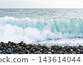 Large ocean wave breaking onto a rocky pebble beach beneath open sky. Coastal seascape and natural water movement. Marine environment, shoreline erosion and ocean power. Copy space 143614044