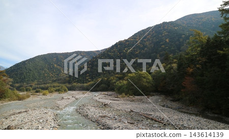 一條河流蜿蜒流經群山,周圍環繞著開始變色的森林,河床寬闊而佈滿石頭。 一條河流蜿蜒流經群山,周圍環繞著開始變色的森林,河床寬闊而佈滿石頭。 143614139