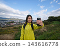 A woman takes a selfie with the mountains and town visible from the Shibusawa Hills as a backdrop. 143616778