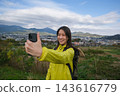 A woman takes a selfie with the mountains and town visible from the Shibusawa Hills as a backdrop. 143616779
