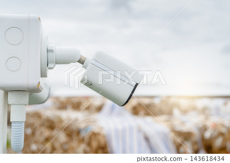 White CCTV security camera monitoring a paper recycling factory outdoors in daylight, video surveillance system protecting industrial operations, property, workers and recyclable material White CCTV security camera monitoring a paper recycling factory outdoors in daylight, video surveillance system protecting industrial operations, property, workers and recyclable material 143618434