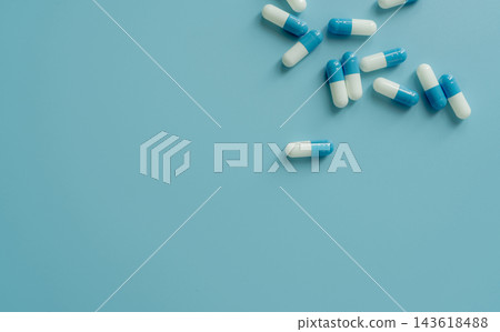 Blue and white antibiotic capsule pills on blue background with copy space, top view concept for prescription medication, pharmaceutical care, antimicrobial treatment and drug resistance awareness. Blue and white antibiotic capsule pills on blue background with copy space, top view concept for prescription medication, pharmaceutical care, antimicrobial treatment and drug resistance awareness. 143618488