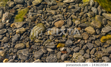 Smooth river stones beneath clear shallow water with green algae and natural textures in a rocky streambed landscape Smooth river stones beneath clear shallow water with green algae and natural textures in a rocky streambed landscape 143619384