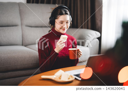 Young adult asian woman using laptop relax sitting in cozy winter living room with christmas tree enjoy alone at home for the holidays Young adult asian woman using laptop relax sitting in cozy winter living room with christmas tree enjoy alone at home for the holidays 143620041