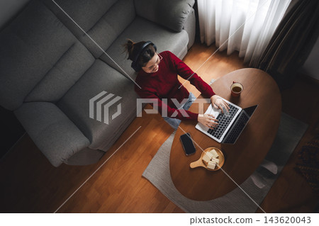 Asian woman using laptop on side table remote work from home for the holidays relax sitting in cozy living room Asian woman using laptop on side table remote work from home for the holidays relax sitting in cozy living room 143620043