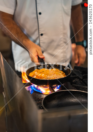 A chef in a white jacket cooks a small skillet on a gas range at a Maldives resort, creamy orange sauce with seafood simmers, warm lighting, shallow depth of field. A chef in a white jacket cooks a small skillet on a gas range at a Maldives resort, creamy orange sauce with seafood simmers, warm lighting, shallow depth of field. 143620170