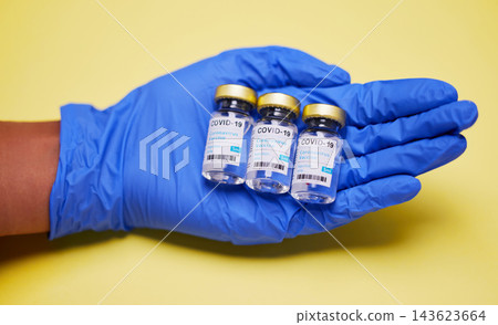 Hand, gloves and vaccine or vial in studio for wellness, healthcare and safety from disease. Medical worker, ppe and innovation by yellow background for protection, prevention and viral defence 143623664