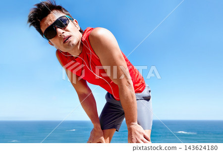 Runner, man and tired with earphones at beach with rest, break or breathing with music in summer sunshine. Person, listening and streaming with subscription with workout, memory and fitness by ocean Runner, man and tired with earphones at beach with rest, break or breathing with music in summer sunshine. Person, listening and streaming with subscription with workout, memory and fitness by ocean 143624180