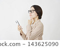 A middle-aged businesswoman thinking with her smartphone in hand, against a white background. 143625090