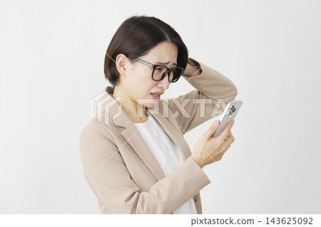 一位中年女商人，手裡拿著智慧型手機，雙手抱頭，背景是白色。 143625092