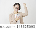 A middle-aged businesswoman looks at her smartphone and makes a triumphant gesture against a white background. 143625093