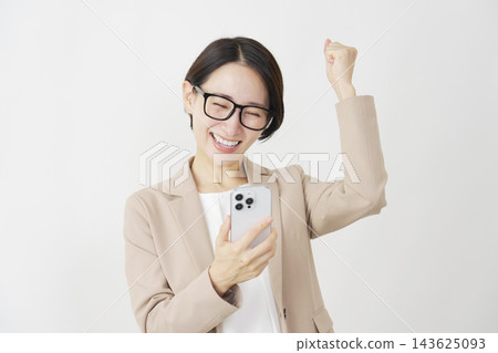 一位中年女商人看著她的智慧型手機，在白色背景前做出了一個勝利的手勢。 143625093