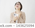 A middle-aged businesswoman looks at her smartphone and makes a triumphant gesture against a white background. 143625094