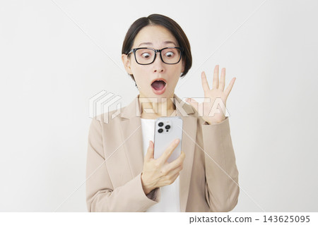 一位中年女商人對著白色背景下的智慧型手機，臉上露出驚訝的表情。 143625095