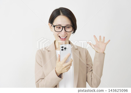 一位中年女商人舉著智慧型手機，對著白色背景露出驚訝的笑容。 143625096