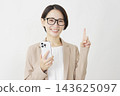 A middle-aged businesswoman holding a smartphone and pointing to the right; white background. 143625097