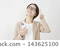 A middle-aged businesswoman holding a smartphone and pointing upwards against a white background. 143625100