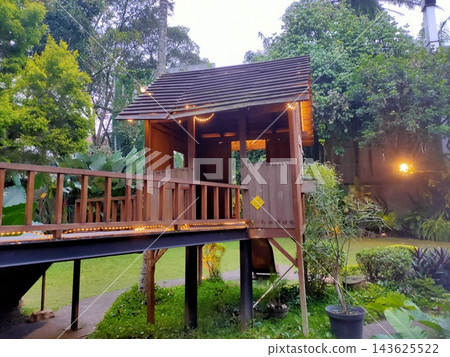Cozy wooden treehouse with lights in lush garden Cozy wooden treehouse with lights in lush garden 143625522