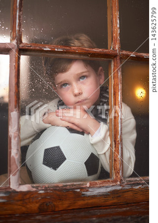 Thinking, sad and kid by window with soccer ball for playing outdoor, frustrated and waiting for rain. Bored, lonely and young boy by glass with football for mental health and psychology in home Thinking, sad and kid by window with soccer ball for playing outdoor, frustrated and waiting for rain. Bored, lonely and young boy by glass with football for mental health and psychology in home 143625799