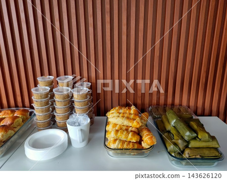 Catering food spread with baked pastries, dessert cups, and traditional banana leaf snacks 143626120