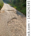 Severely broken rural road surface showing deep potholes and cracked asphalt 143626345