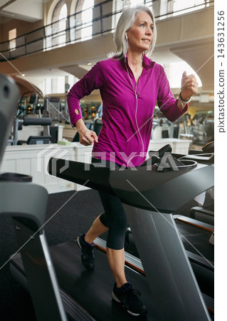Woman, running on treadmill and training by music in gym club, breathing and cardio for health in wellness. Mature, female runner and exercise with podcast, athlete and workout by speed machine Woman, running on treadmill and training by music in gym club, breathing and cardio for health in wellness. Mature, female runner and exercise with podcast, athlete and workout by speed machine 143631256