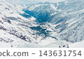 Panoramic snowy alpine valley with ski resort village nestled between towering snow-covered peaks in bright winter daylight and mo 143631754