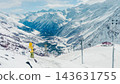 Skier in yellow jacket standing on snowy ridge overlooking steep ski slope, chairlift, and expansive Caucasus mountain valley 143631755