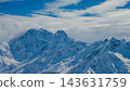 Mount Elbrus and neighboring snow-covered Caucasus peaks beneath blue sky with layered clouds 143631759