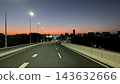 A city highway with a sunset sky and a continuous stretch of streetlights 143632666