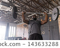 Adult African American man in gymwear pressing barbell overhead at warehouse gym with windows, rig 143633288