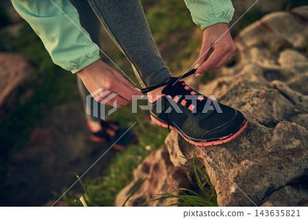 Person, hands and tying shoe with rock of hiker for morning walk or trekking on outdoor mountain. Closeup of human getting ready, preparation or tie laces for hiking, journey or exercise in nature Person, hands and tying shoe with rock of hiker for morning walk or trekking on outdoor mountain. Closeup of human getting ready, preparation or tie laces for hiking, journey or exercise in nature 143635821