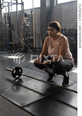 African American woman crouching on mat in gym near loaded barbell wearing tanktop fitness watch African American woman crouching on mat in gym near loaded barbell wearing tanktop fitness watch 143636251