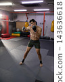 Practicing shirtless fighter wearing green shorts, wraps striking in MMA gym with cage and bags 143636618