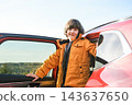 Smiling boy standing by open red car door during family autumn road trip. Child traveler in jacket outdoors. Vacation and journey concept 143637650