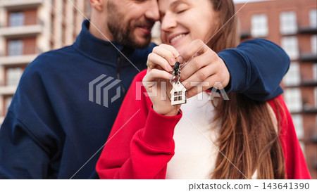Closeup Happy Couple Embracing And Holding Keys With House Keychain Outside Apartment Building. First Home Purchase, Mortgage, Homeownership And Shared Achievement Concept. Closeup Happy Couple Embracing And Holding Keys With House Keychain Outside Apartment Building. First Home Purchase, Mortgage, Homeownership And Shared Achievement Concept. 143641390