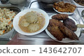 A close-up of a self-service buffet line featuring white bowls of meatballs in a creamy gravy, and plates of dark fried cutlets, alongside metal trays of mixed vegetable rice. A functional canteen mea 143642707