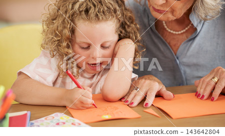 Grandmother helping granddaughter drawing on orange paper Grandmother helping granddaughter drawing on orange paper 143642804
