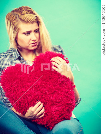 Sad woman holding red pillow in heart shape Sad woman holding red pillow in heart shape 143643103