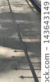 A spiked metal fence casts a linear shadow on a paved walkway. 143643149